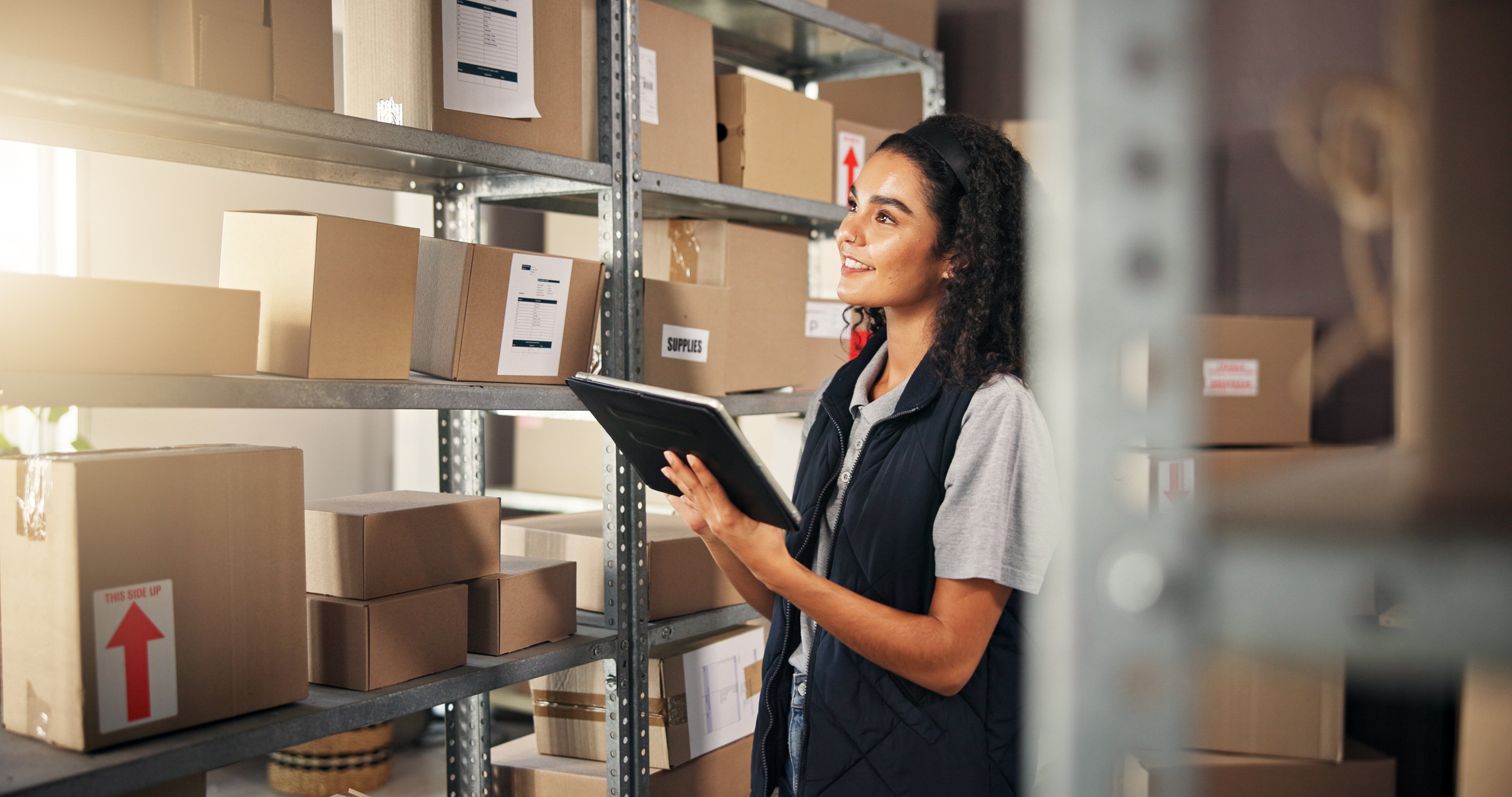 Warehouse management for small business - työntekijä käyttää tablettia varastosaldojen hallintaan hyllyjen äärellä